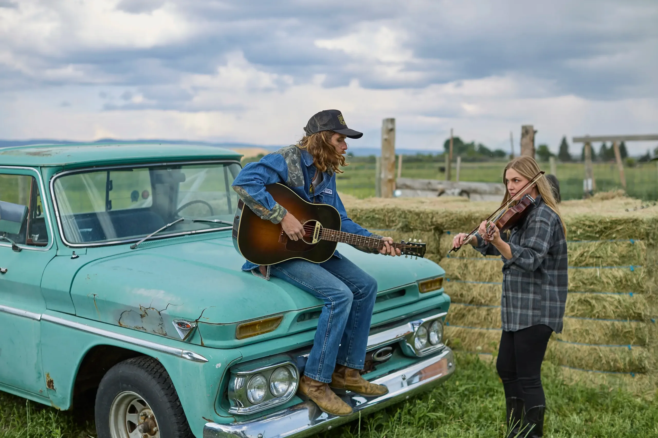 A couple playing a guitar and a violin in front of a field