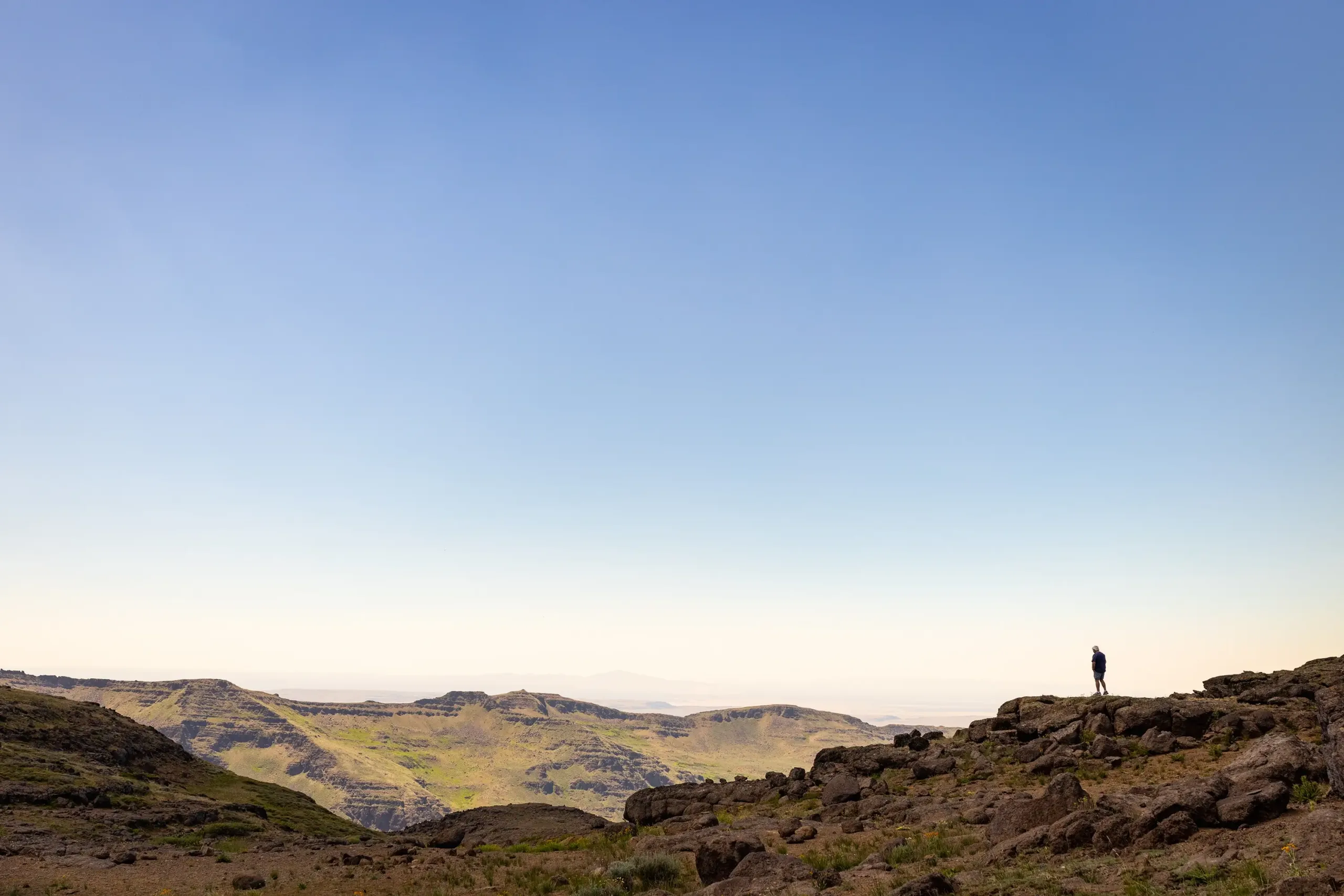 A distant landscape shot of a man walking the skyline of mountain tops