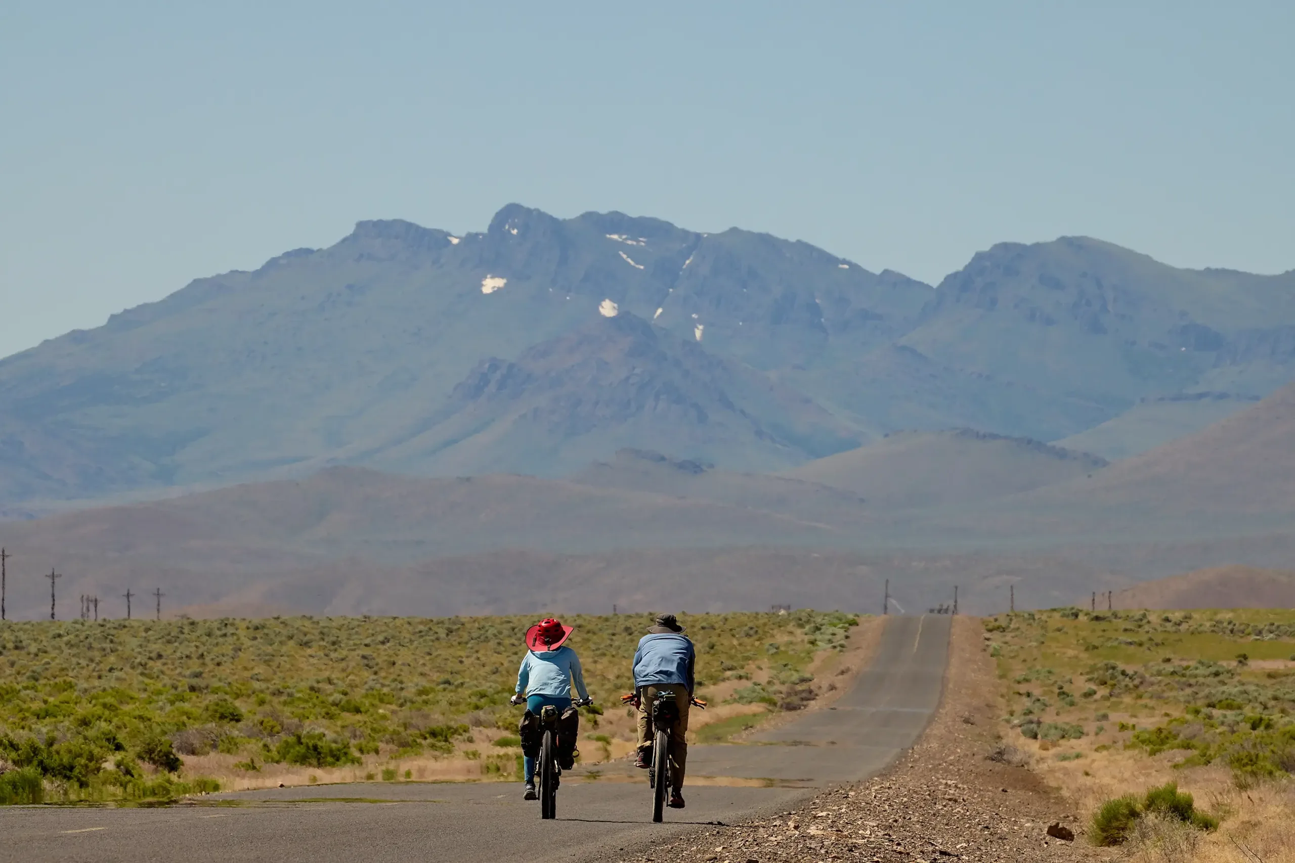Two bicyclists riding a road overlooking mountain peaks